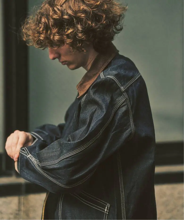 Side view of model wearing a dark indigo Lee work jacket with brown corduroy collar and prominent white contrast stitching.