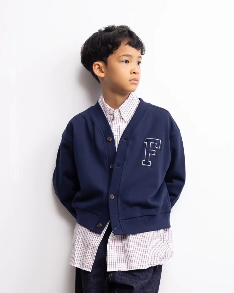 Boy in navy F-logo cardigan over a checker shirt look aside against a plain white background
