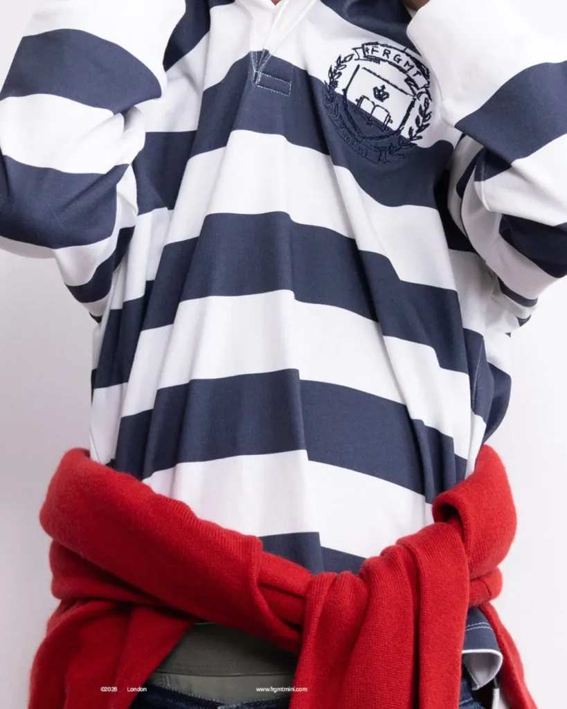 Close-up of navy-white striped rugby with FRGMT crest and red sweater tied around the waist.