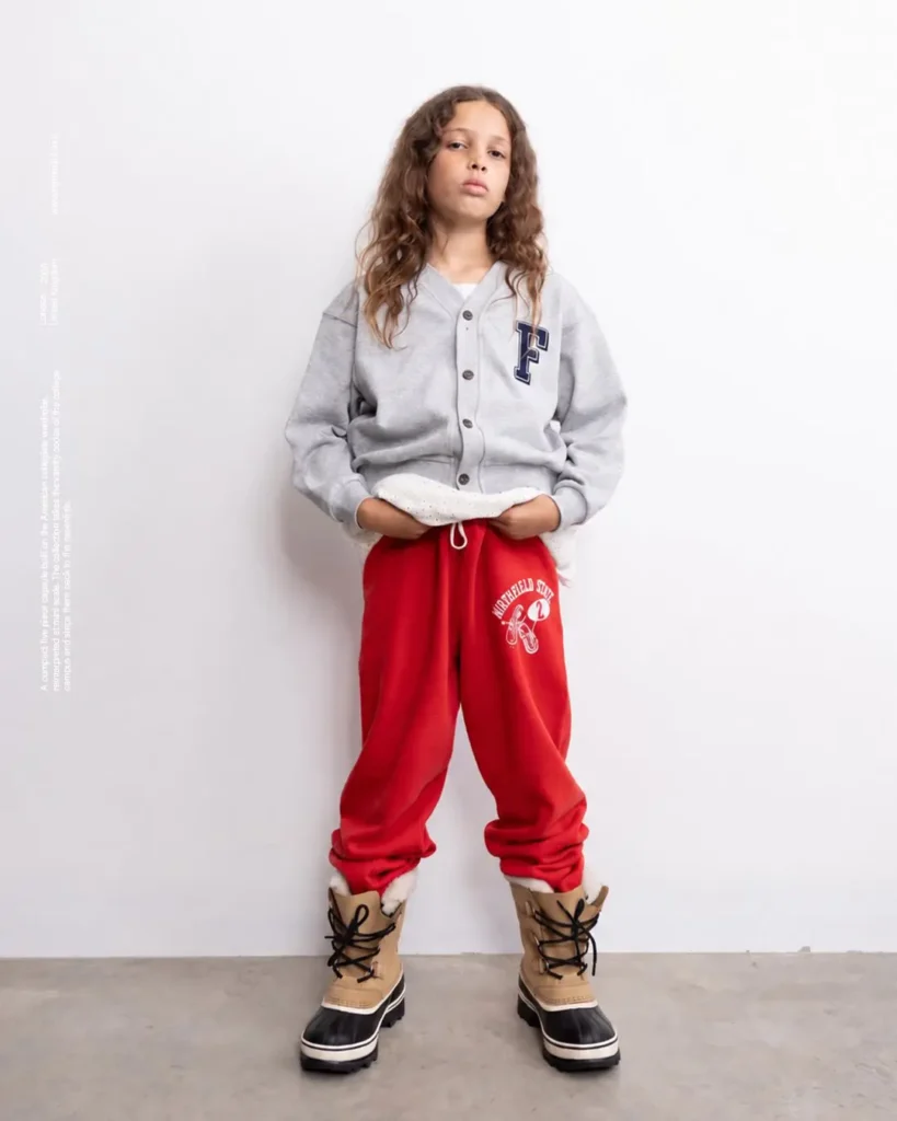 Girl in grey F-logo cardigan, red Northfield State sweatpant, and tan winter boot stand by a white wall