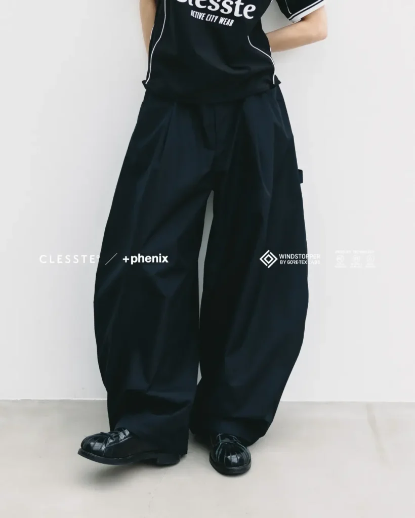 Front-facing view of a model's lower body wearing black balloon-fit utility pants with a smooth barrel silhouette, paired with a black "CLESSTE Active City Wear" T-shirt and black woven loafer