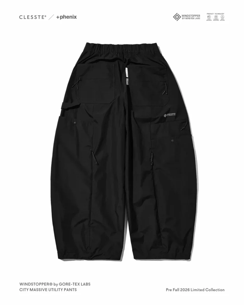 Back view of black balloon-fit utility pants showing two flap chest pockets with drawcord pulls, rear cargo pockets with snap closures, and center back seam, laid flat on white background