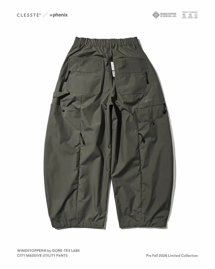 Back view of olive/dark green balloon-fit utility pants showing two flap chest pockets with drawcord pulls, rear cargo pockets with snap closures, and center back seam, laid flat on white background