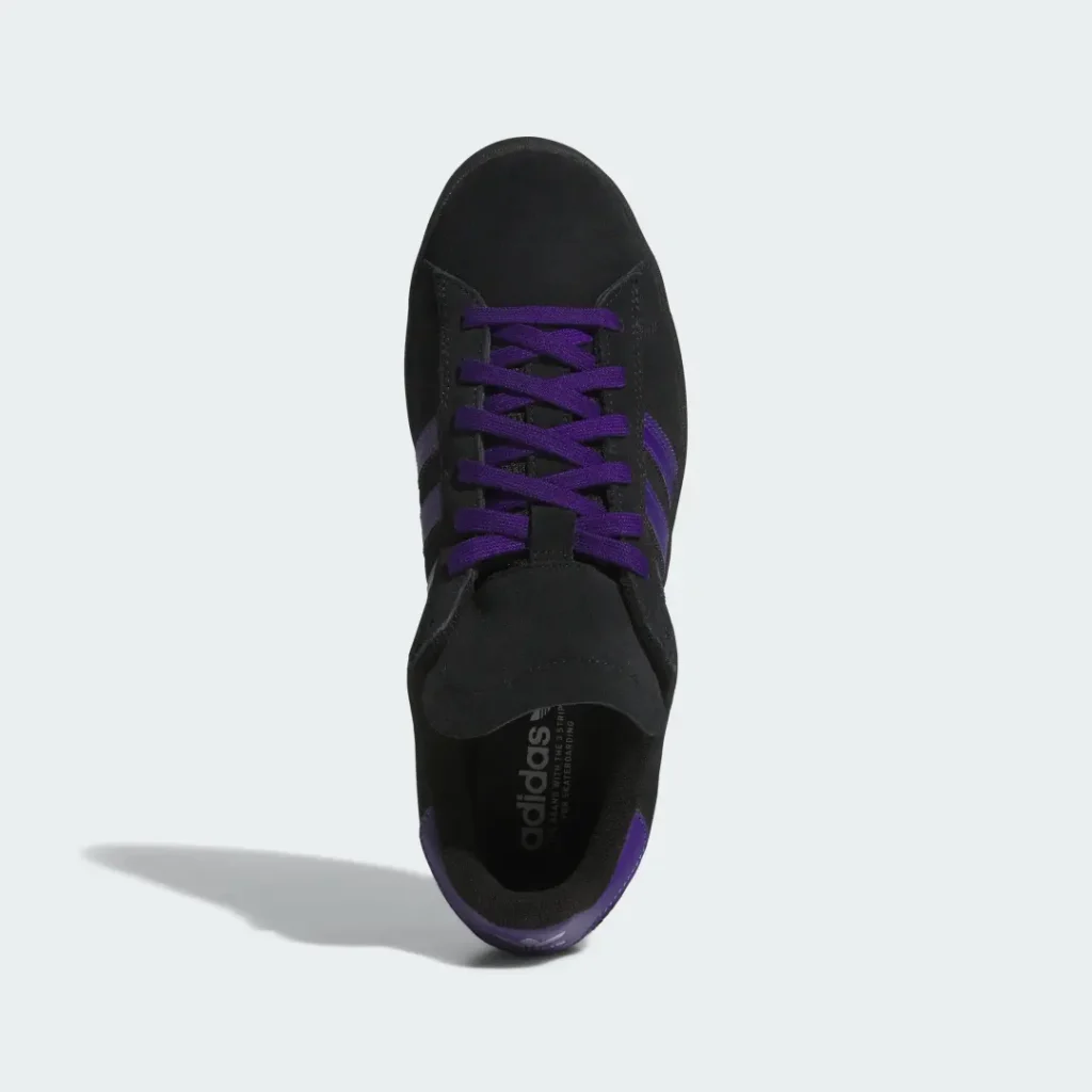 Black sneaker viewed from above, with purple laces and side stripes, casting a long shadow on a pale background
