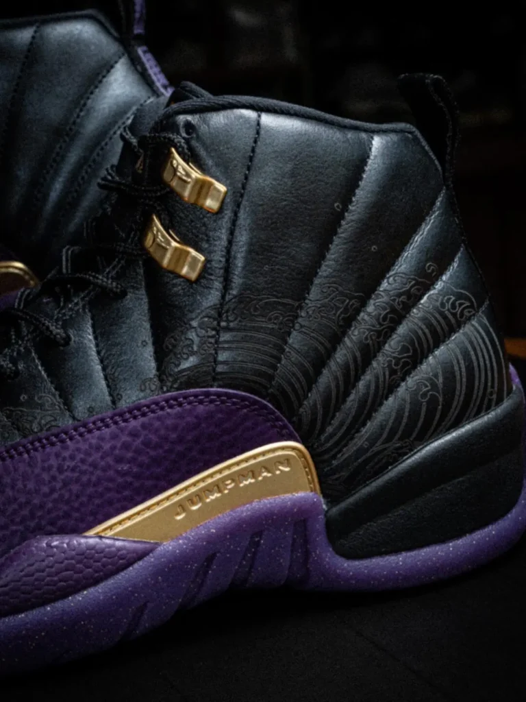 Close-Up Of The Air Jordan 12 Feature Black Leather, Tonal Wave Patterns Purple Texture Mudguard, And Gold Jumpman Side Plate