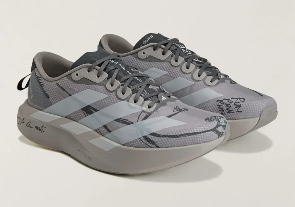 Pair of gray adidas Adizero running shoes with pale three-stripe branding, black sketch graphics, and handwritten detail