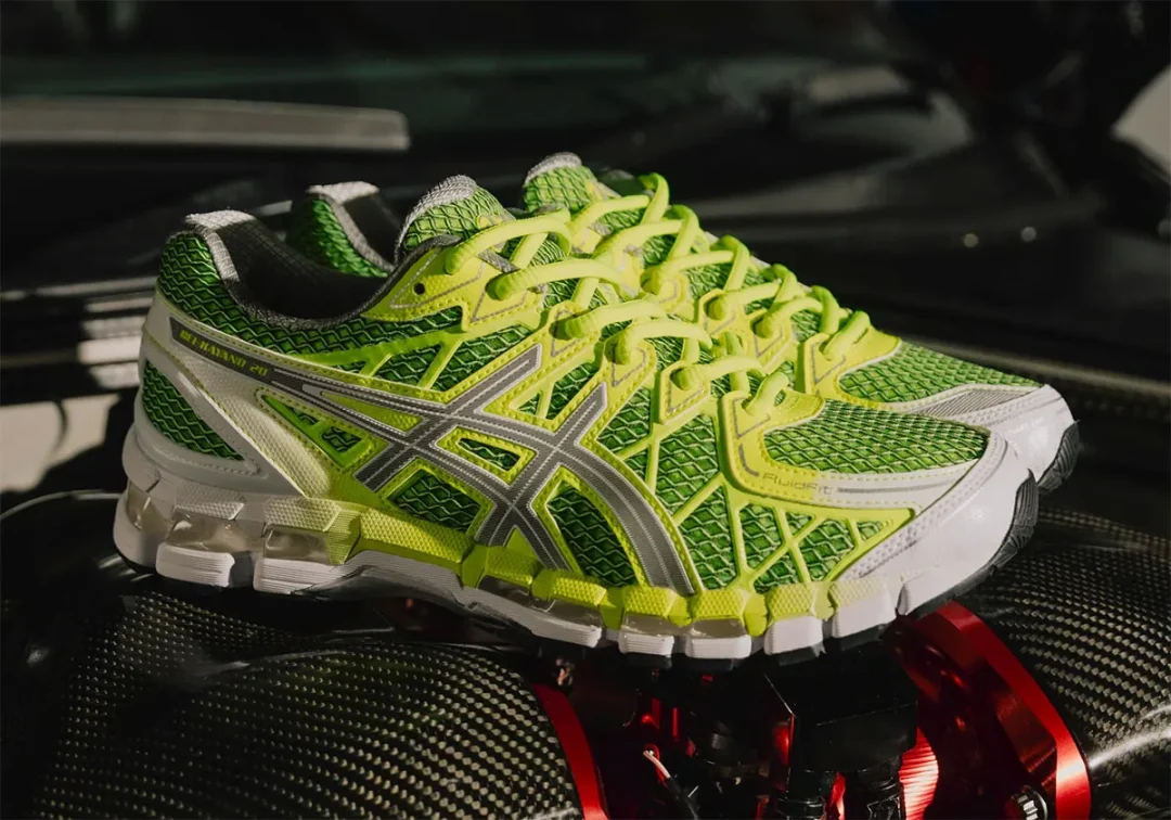 ASICS GEL-Kayano 20 in bright green, silver and white resting on a carbon-fiber automotive component.