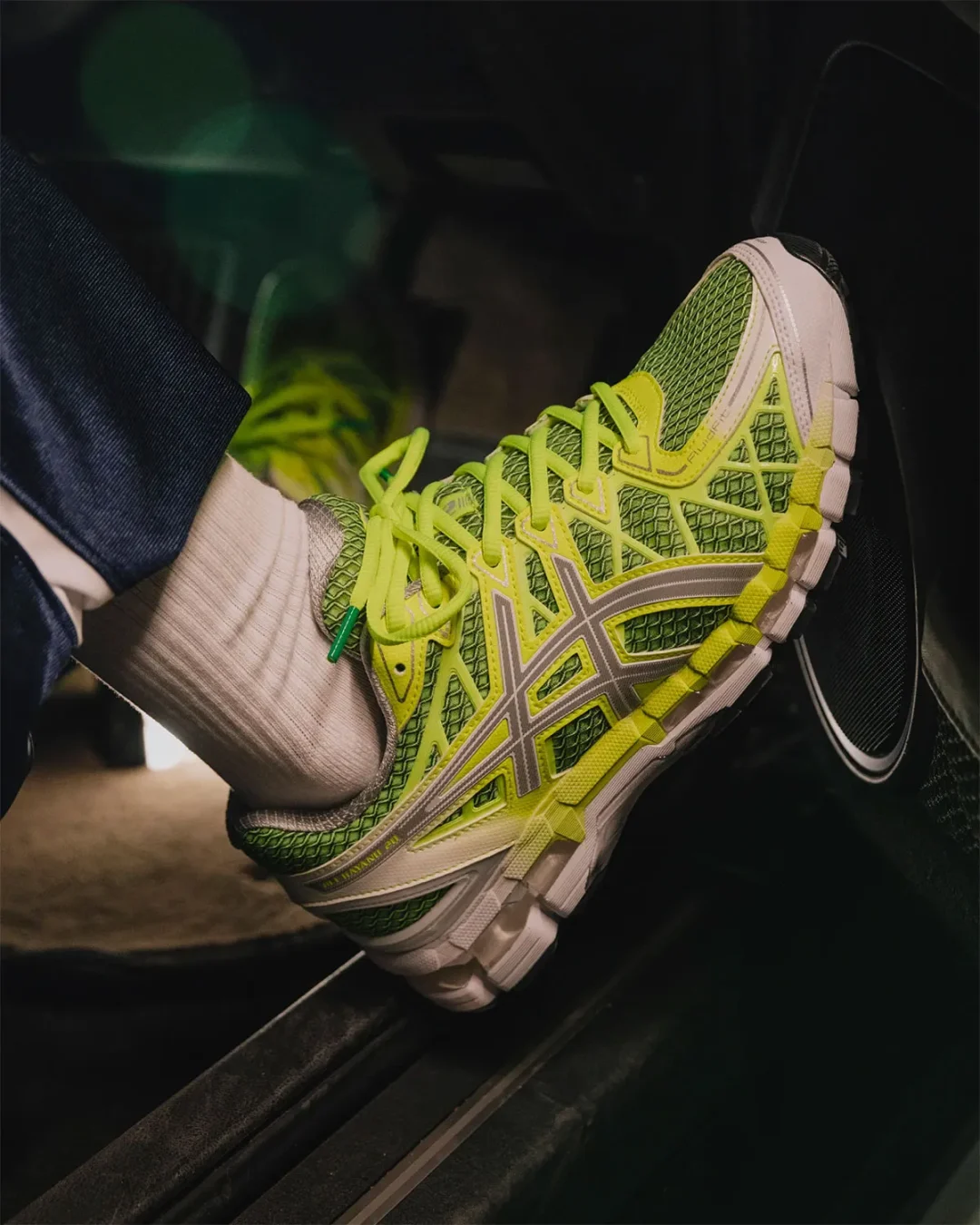 ASICS GEL-Kayano 20 in bright green, silver and white worn inside a car.