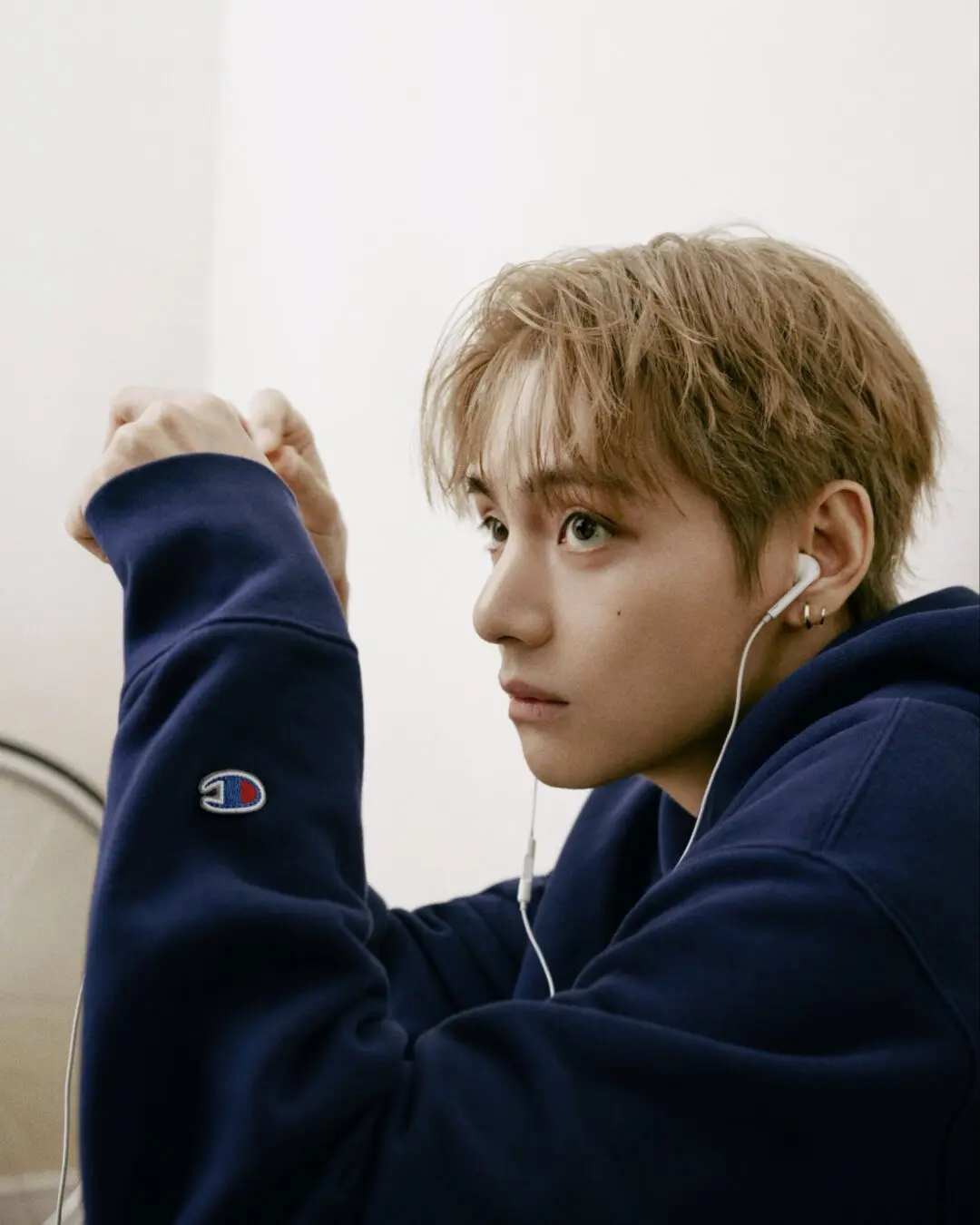 Close-up portrait of a person in a navy Champion hoodie wearing white wired earphones, with the embroidered Champion logo visible on the sleeve.