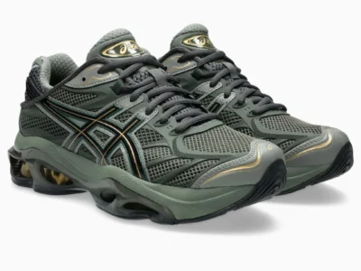 Pair of dark olive ASICS show shoe shown from the front angle, highlighting the mesh toe box, black laces, metallic gold branding, and oversized cushion sole