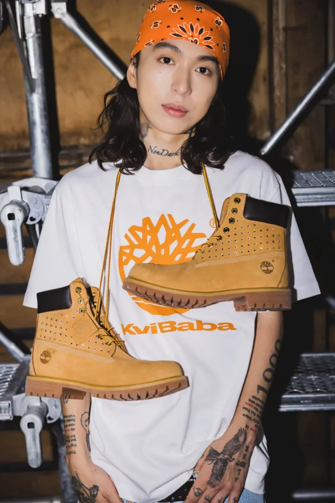 Model wear an orange bandana and white Timberland x Kvi Baba graphic Tee with wheat boot display across the torso
