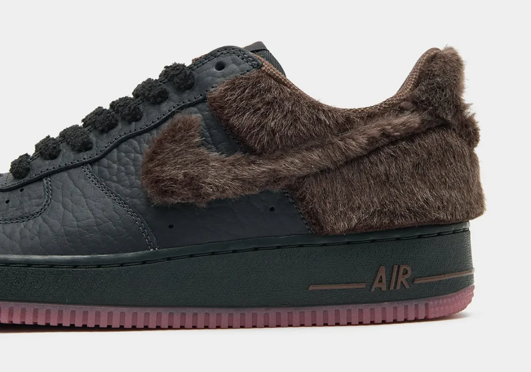 Close-up of a black leather shoe with brown faux-fur Swoosh and collar, dark sole, and translucent pink outsole on white