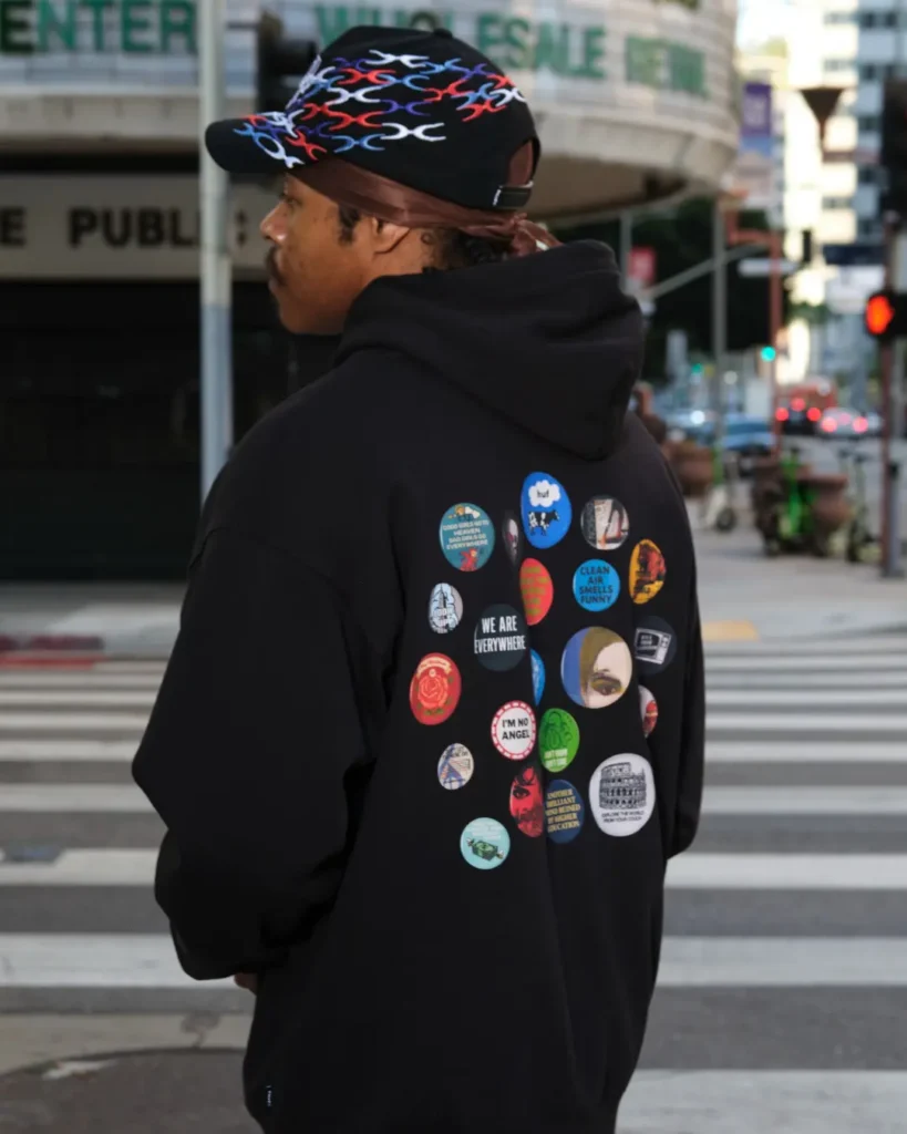 Rear view of a model in a black HUF hoodie decorated with a collection of colorful circular graphic patch