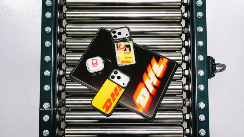 DHL-branded phones, tablet, and access badge arranged on a black case atop metal conveyor rollers