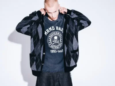 Model wear a black-and-gray argyle cardigan over a distressed Mastermind x BAPE skull-logo graphic top with dark wide-leg jean