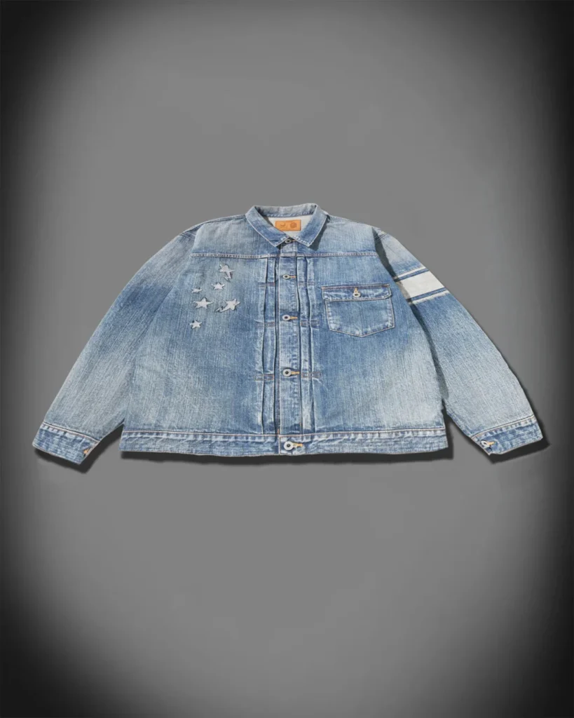 Front product view of a faded blue denim jacket with star appliqués, contrast sleeve stripes and chest pocket on a gray background
