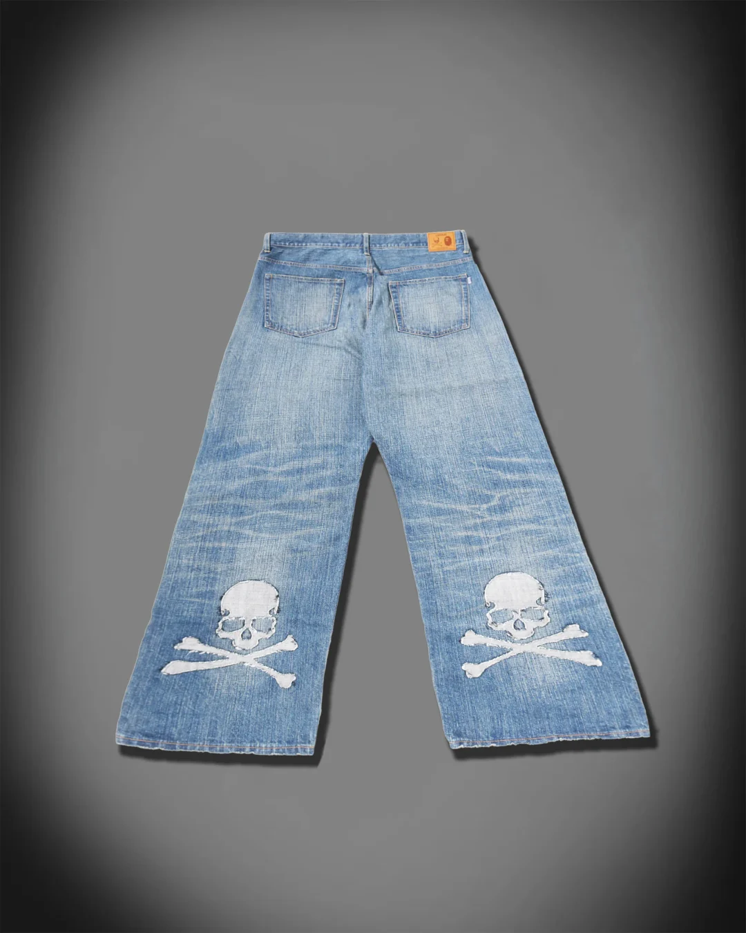 Back view of faded wide-leg blue jeans featuring large skull-and-crossbones appliqués near the lower legs.