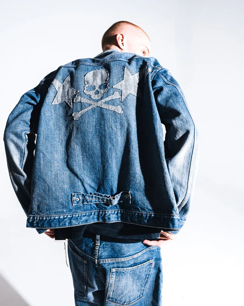 Rear view of an oversized blue denim jacket featuring a large skull-and-crossbones graphic framed by star and lightning motif