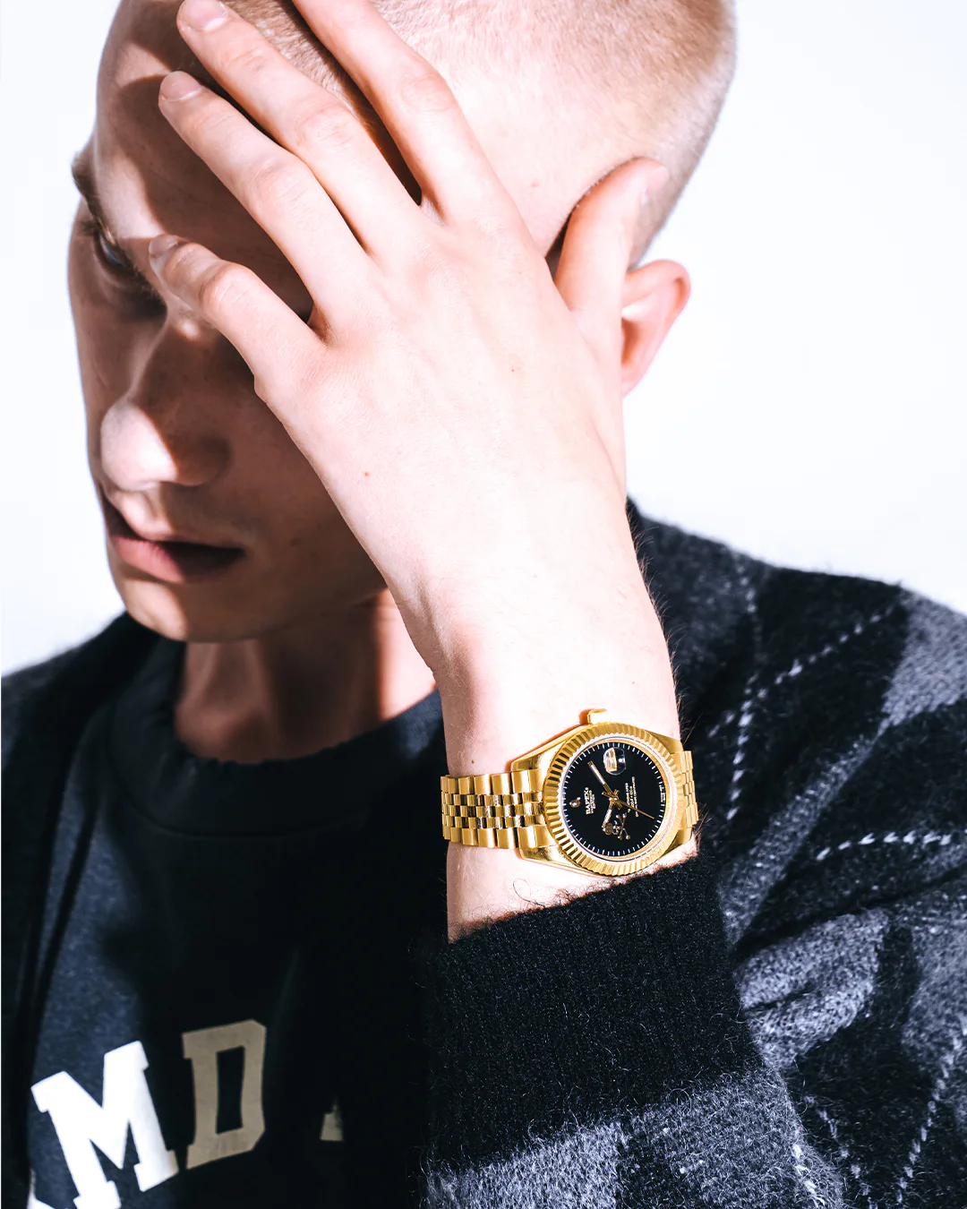 Close-up of model wearing a gold-tone BAPEX watch with black dial alongside a black-and-gray argyle cardigan.