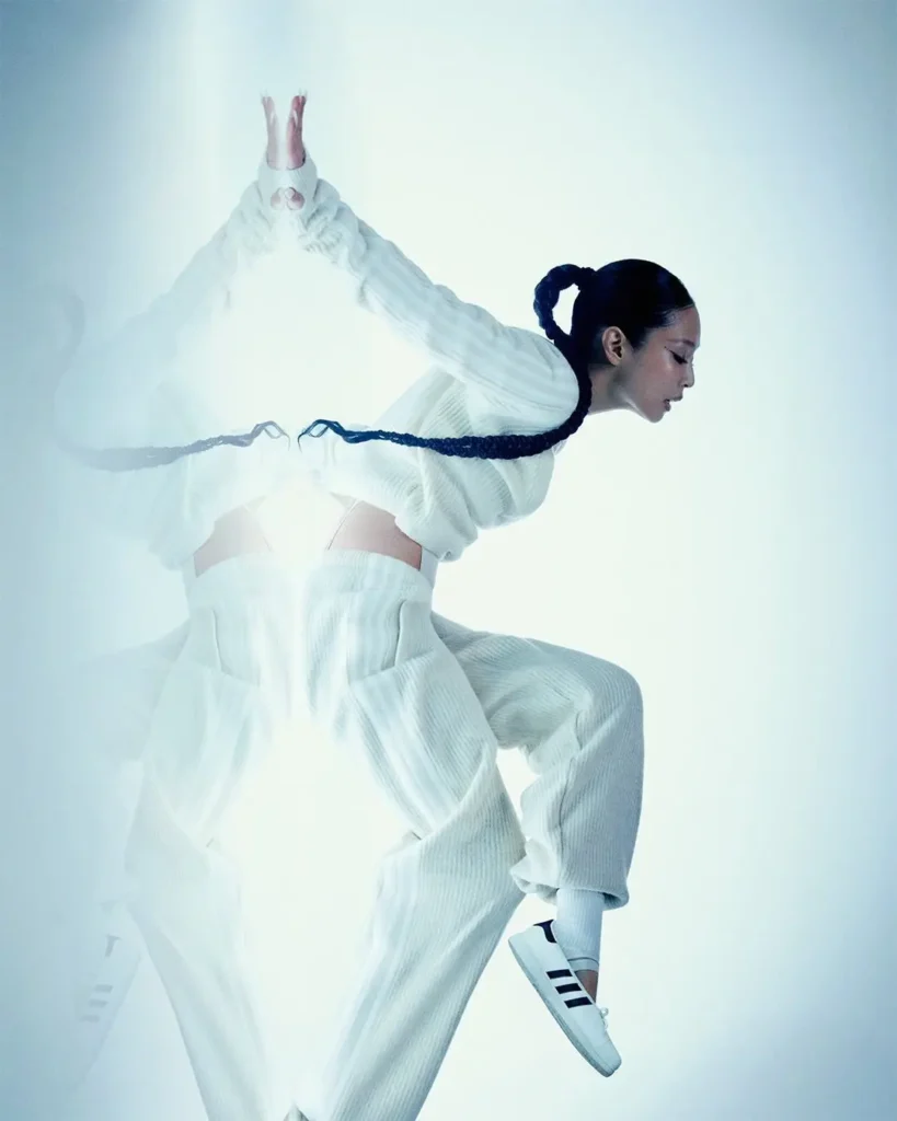 Model Poses In Motion Wearing A Flowing White Outfit And White Adidas Jennie Ballet Shoe