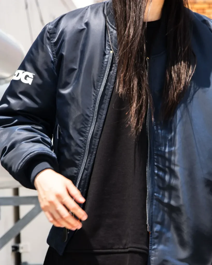 Front view of a black CDG bomber jacket partially unzipped over a black Tee, highlight its clean form, ribbed collar, and zip-front construction