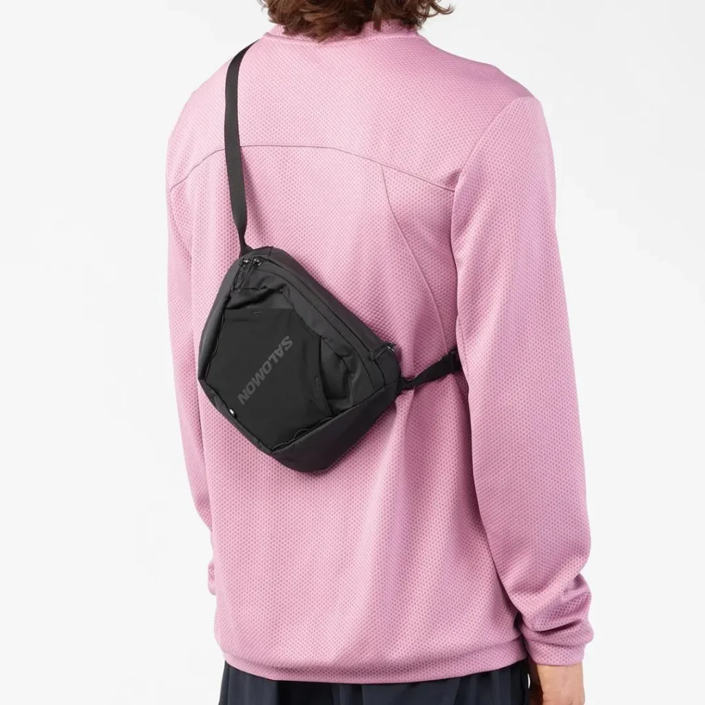 Rear view of the model wearing the black Salomon shoulder bag across the back, showing the adjustable strap system, ergonomic fit, and lightweight everyday carry profile