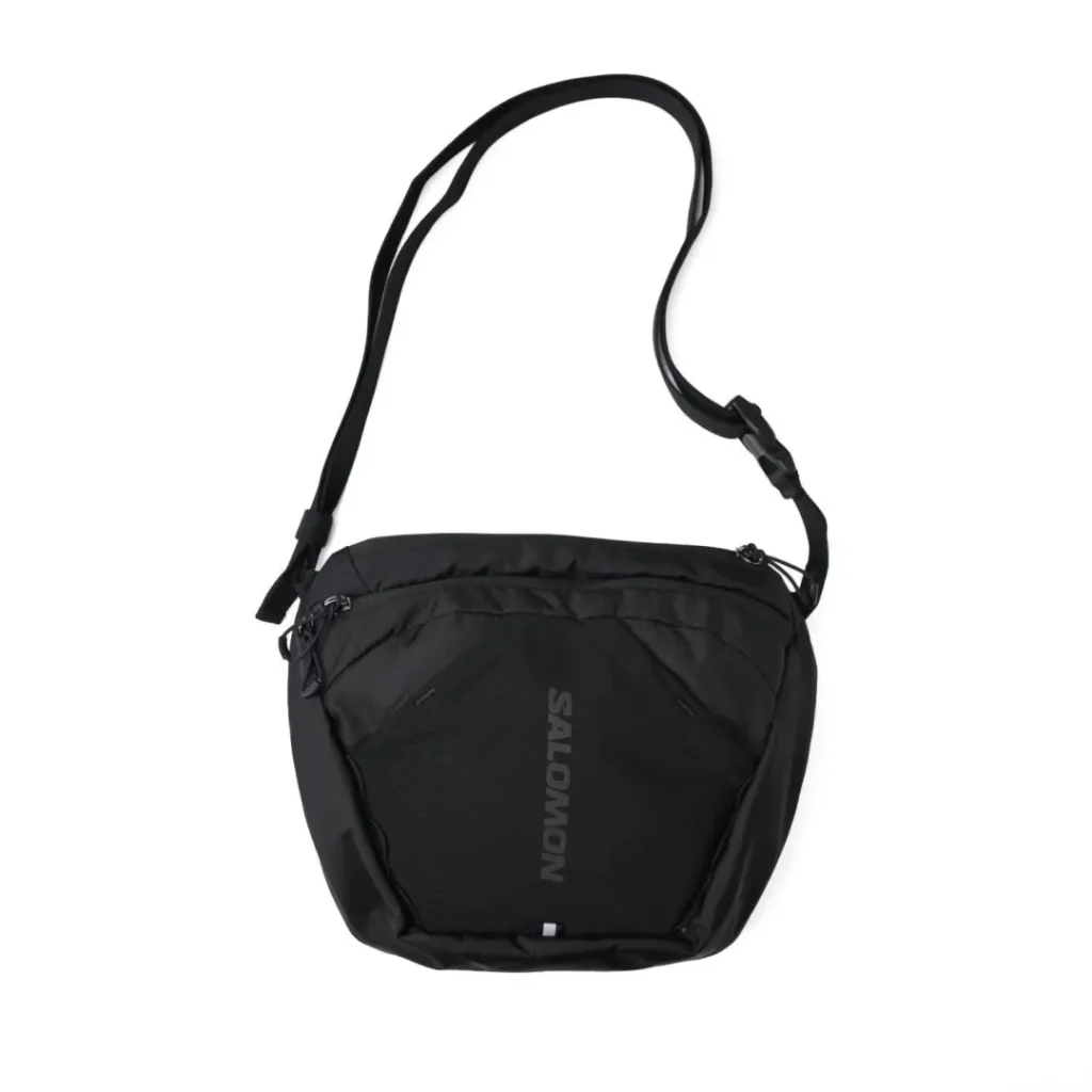 Front studio view of the black Salomon shoulder bag featuring a ripstop nylon body, breathable mesh front panel with tonal Salomon branding, dual-zip main compartment, and adjustable shoulder strap