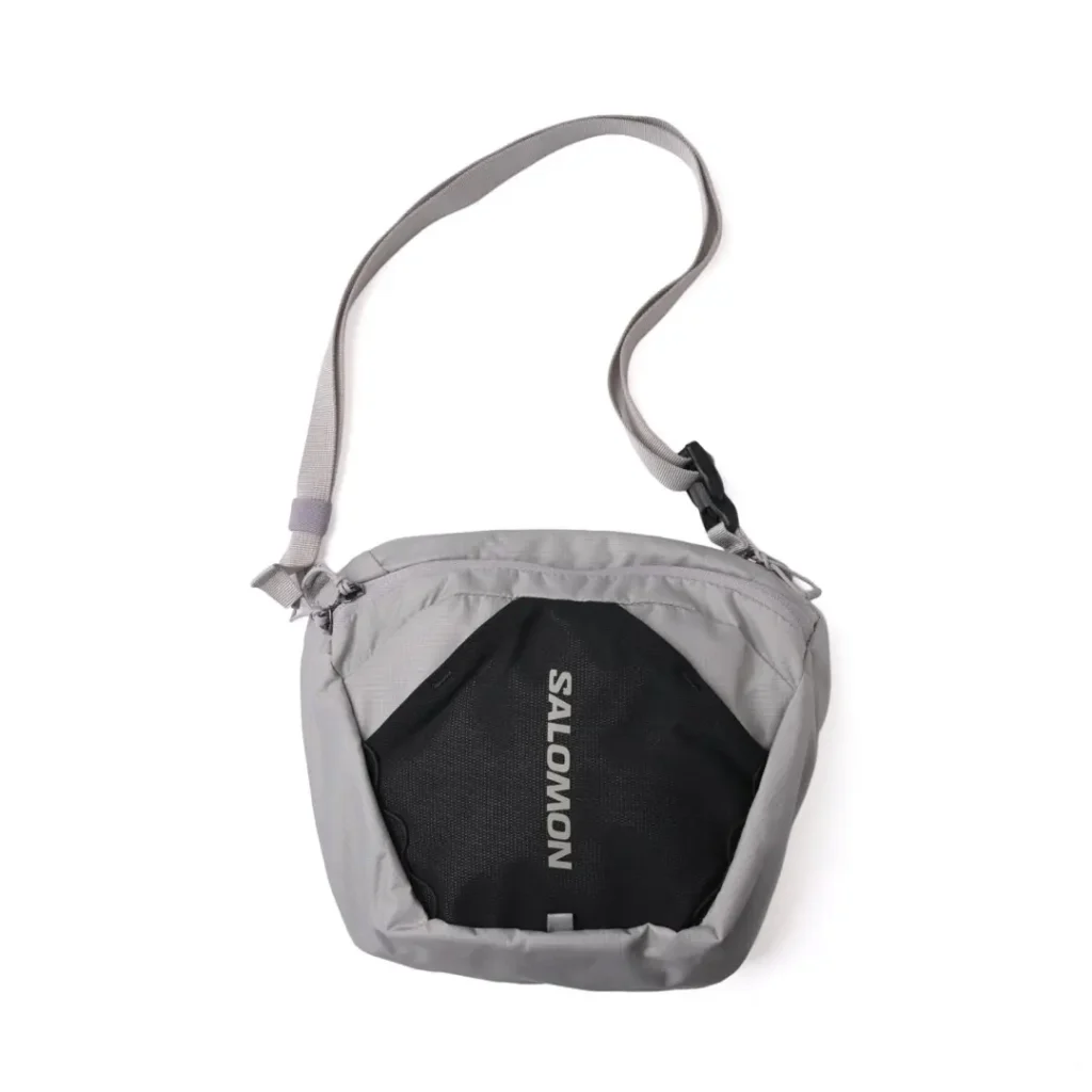 Front view of the gray Salomon shoulder bag combining a light gray ripstop shell with a contrasting black mesh front panel, reflective branding, and an adjustable crossbody strap