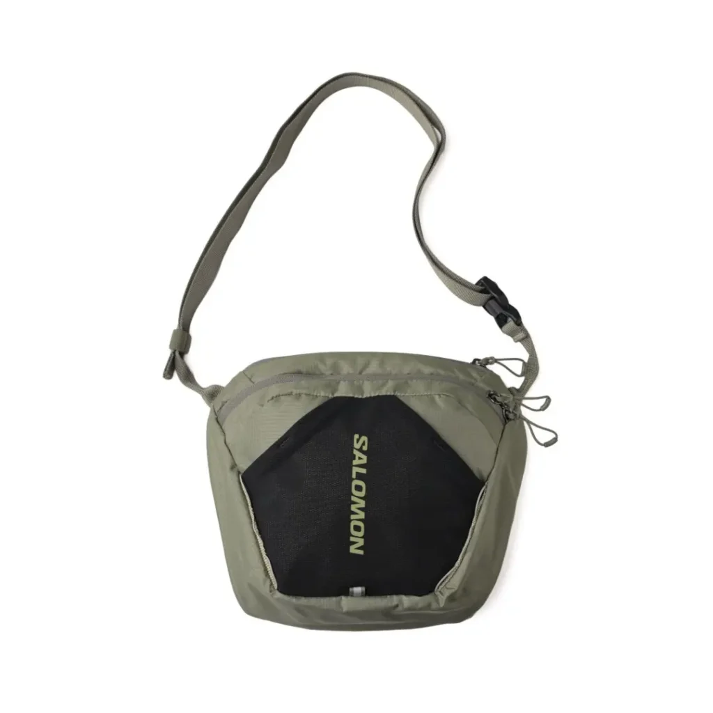 Olive green Salomon shoulder bag with a black mesh front pocket, tonal logo, dual-zip closure, and adjustable shoulder strap designed for lightweight daily use