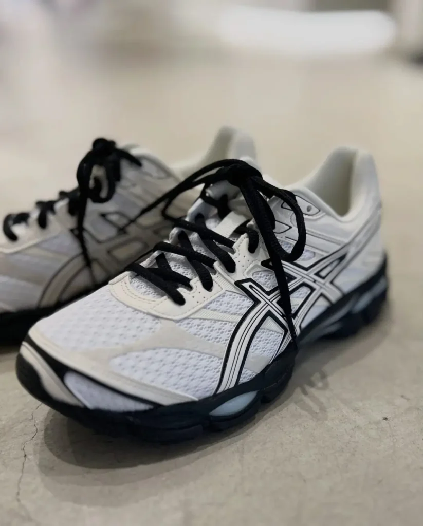 Angled front three-quarter view of the ASICS GEL-CUMULUS 16 featuring breathable white mesh, cream overlays, black laces, and chunky black GEL cushion