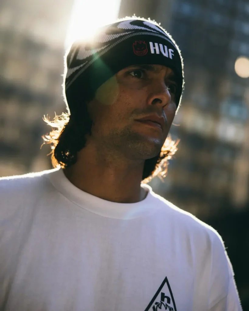 Close-up portrait of a person wearing a black-and-white HUF x Spitfire beanie and white graphic tee in backlit sunlight