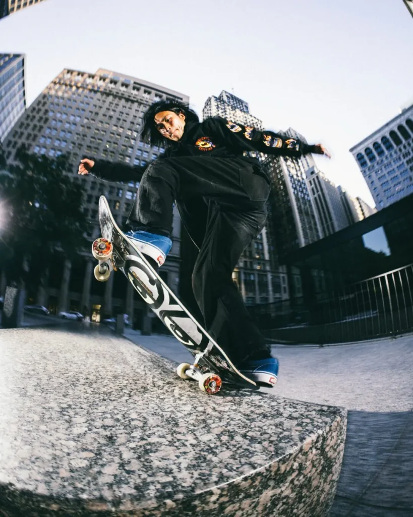 Skateboarder grinds a granite ledge in a downtown plaza while wearing a black HUF x Spitfire hoodie