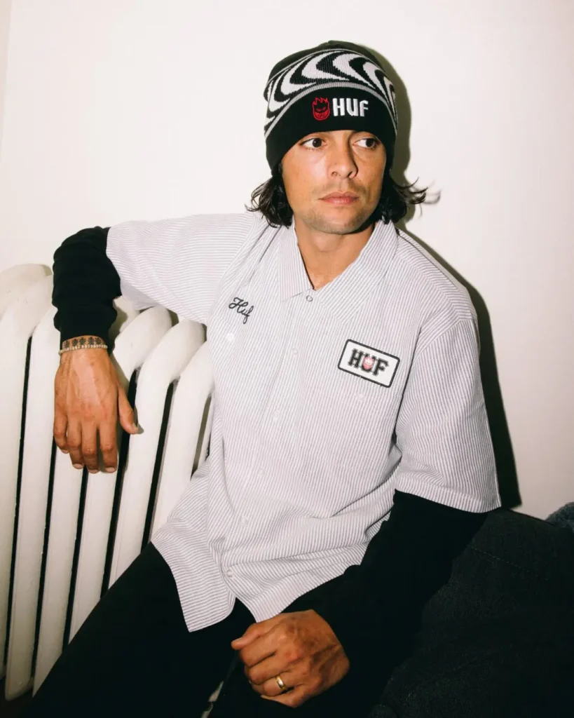 Person wearing a black-and-white HUF x Spitfire beanie and striped HUF work shirt poses beside a radiator
