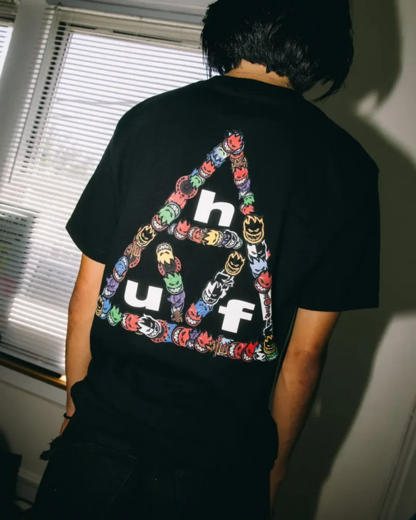Rear view of a black Tee featuring a colorful HUF triangle logo filled with multiple Spitfire flame graphic