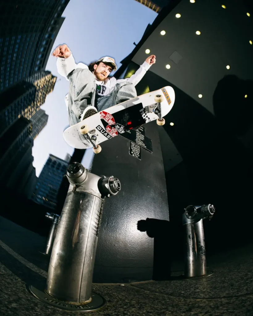 Skateboarder performs an aerial trick above an urban ledge while wearing a HUF x Spitfire sweatshirt and cap
