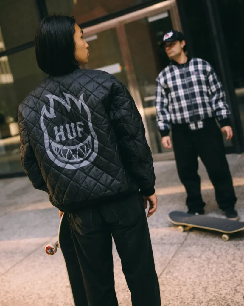 Rear view of a quilted black jacket featuring a large reflective HUF x Spitfire flame logo graphic