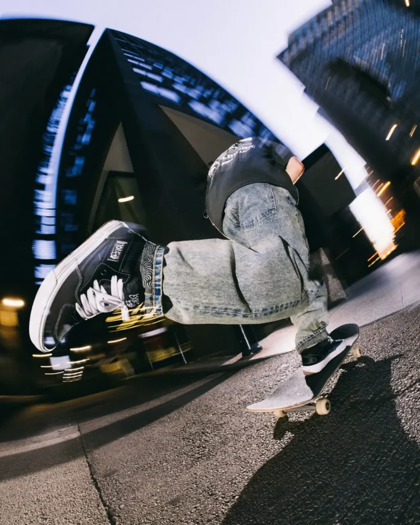 Skateboarder's foot in HUF x Spitfire footwear lands on a board with motion blur against a city backdrop