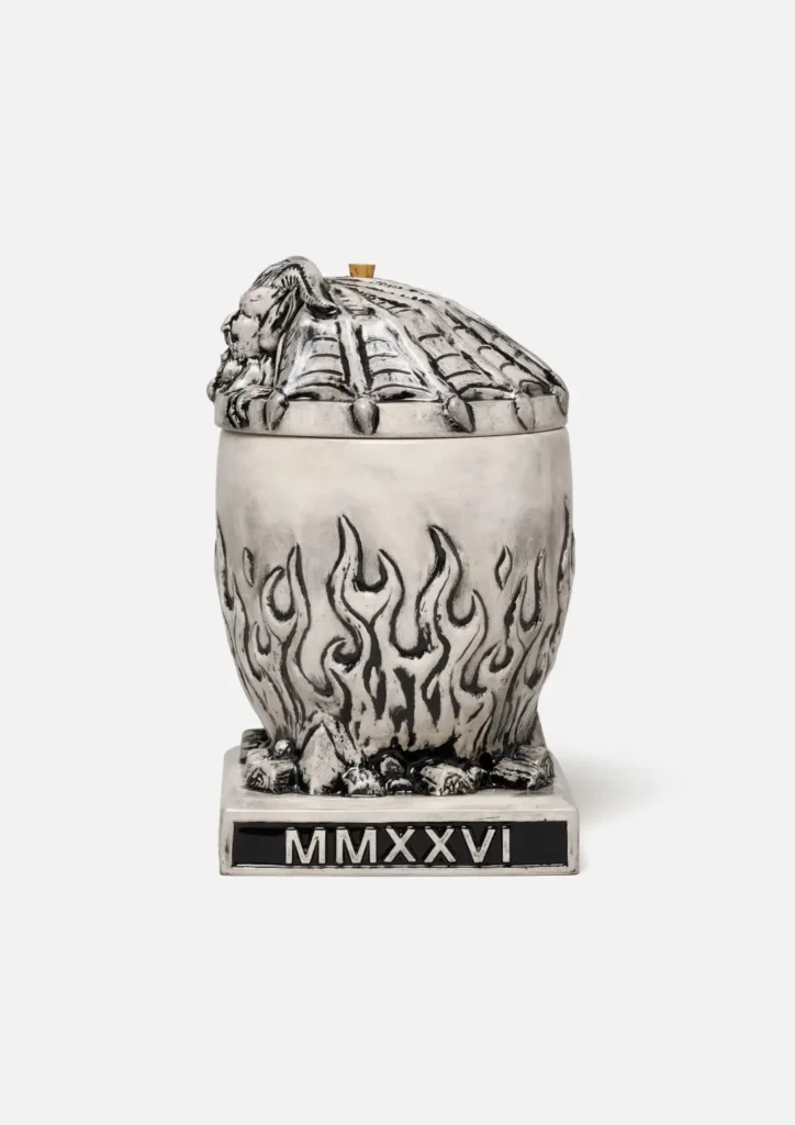 Side view of the same Neighborhood incense chamber. The gargoyle lid is secure on top, show the segment, bat-like rib texture of its back. The flame-pattern body rest on the skull base. The black plaque on the front of the base is engrave with the white Roman numeral "MMXXVI