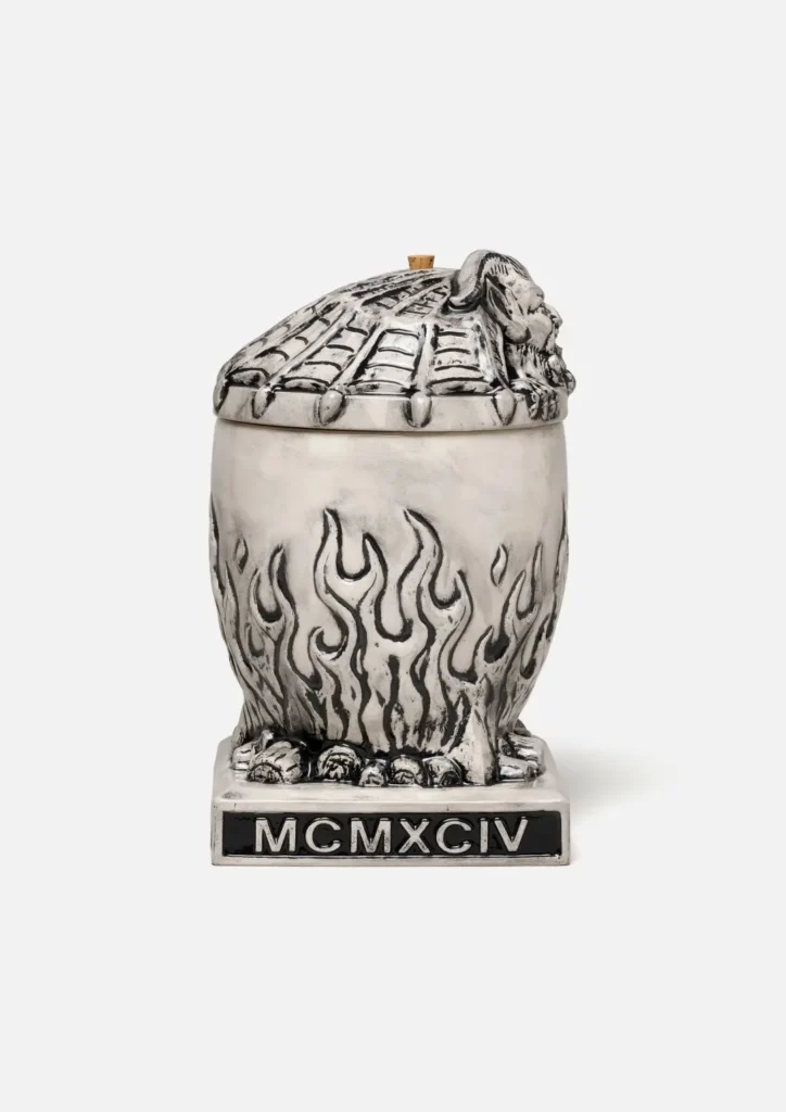 Opposite side view of the Neighborhood incense chamber with the gargoyle lid on top. The flame-pattern body and skull base are visible. The black plaque on the front of the base is engrave with the white Roman numeral "MCMXCIV"