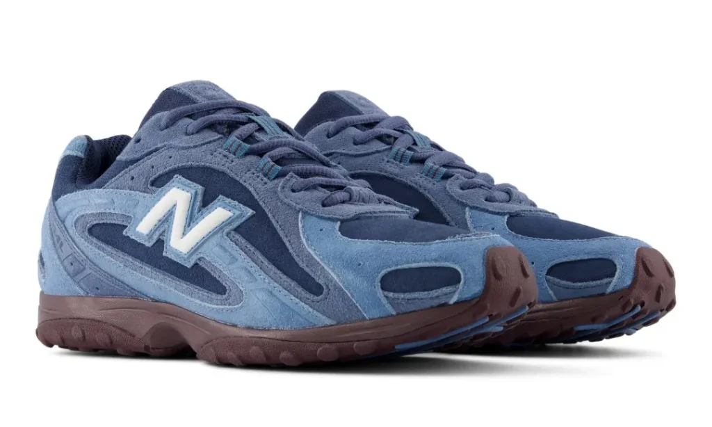Angled product view of blue New Balance shoes on a white background, highlighting white “N” logos, layered suede panels and burgundy outsole
