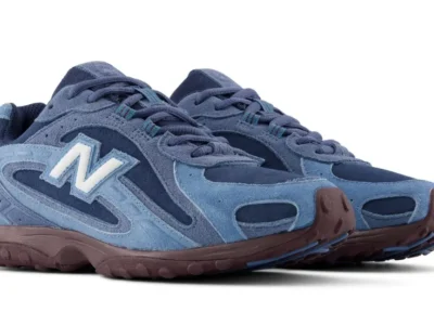 Angled product view of blue New Balance shoes on a white background, highlighting white “N” logos, layered suede panels and burgundy outsole