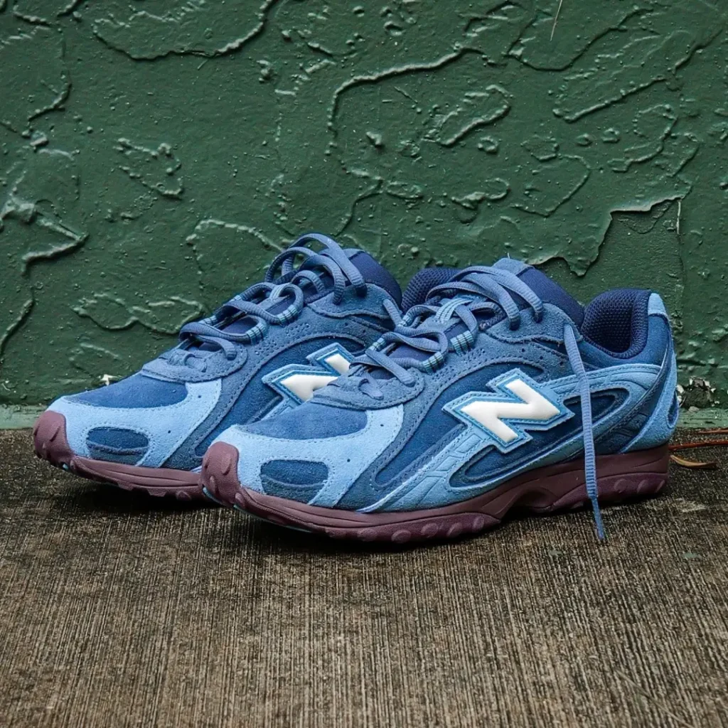 Pair of blue New Balance shoes photographed from the front side, featuring layered suede panels, tonal laces and burgundy sole