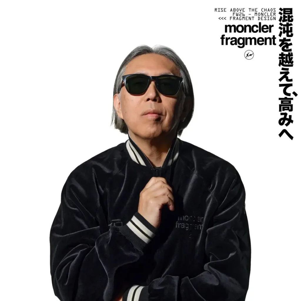 Gray-haired man in sunglasses and black satin varsity jacket, standing against a white background with Moncler Fragment text