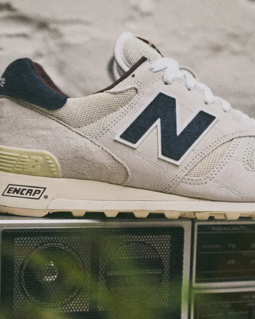 Close-up of the New Balance 1300's toe box and navy N logo show crocodile-emboss suede texture, ENCAP midsole brand, and gum outsole, with a boombox speaker grille below