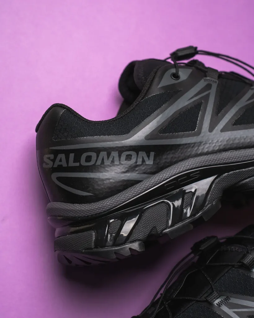 Close-up of a black Salomon trail shoe with gray detailing and rugged sole on a pink background