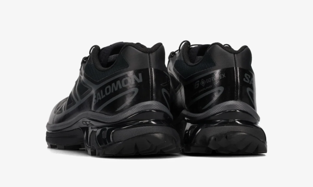 Pair of black Salomon trail shoes shown from the rear, with chunky lugged soles and reflective branding on a white background