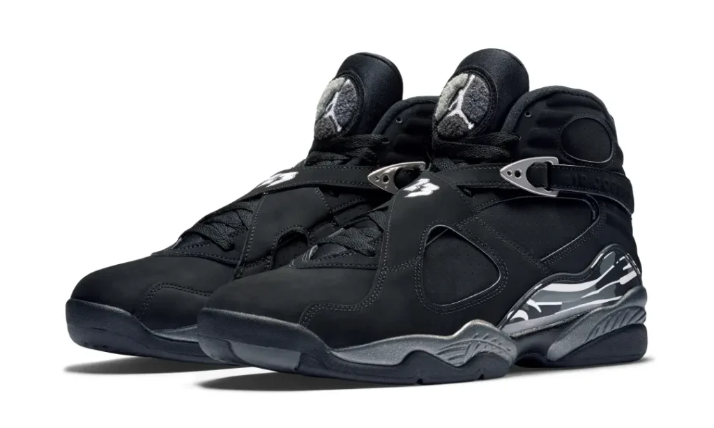 Pair of black Air Jordan 8 shoe with silver buckles and reflective heel panels on a white background
