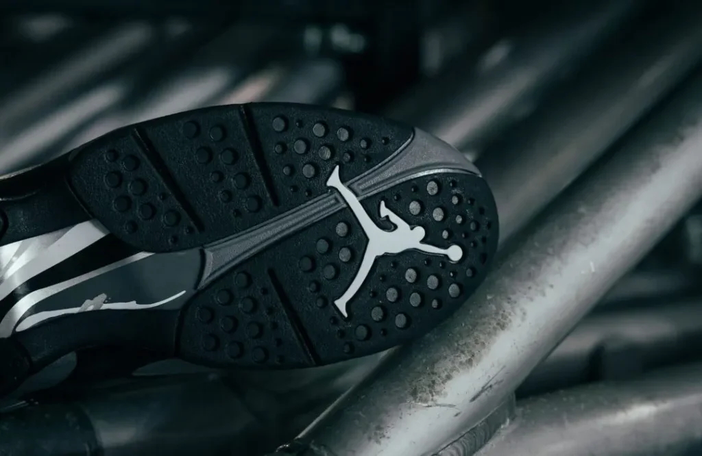 Close-up of a black sneaker sole with circular traction patterns and a white Jumpman logo resting on metal pipes