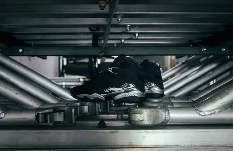 Black high-top shoe with silver accents rest on metal industrial rails beneath a platform