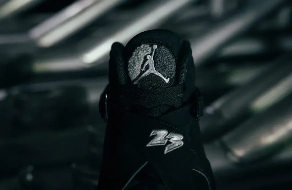 Close-up of a black Air Jordan 8 shoe with a silver Jumpman logo, buckled straps, and silver 23 emblem